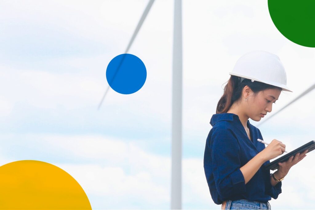 Field worker with wind turbines in the background working on hand held device.