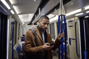 Male business professional standing on subway looking at smart phone mobile device.