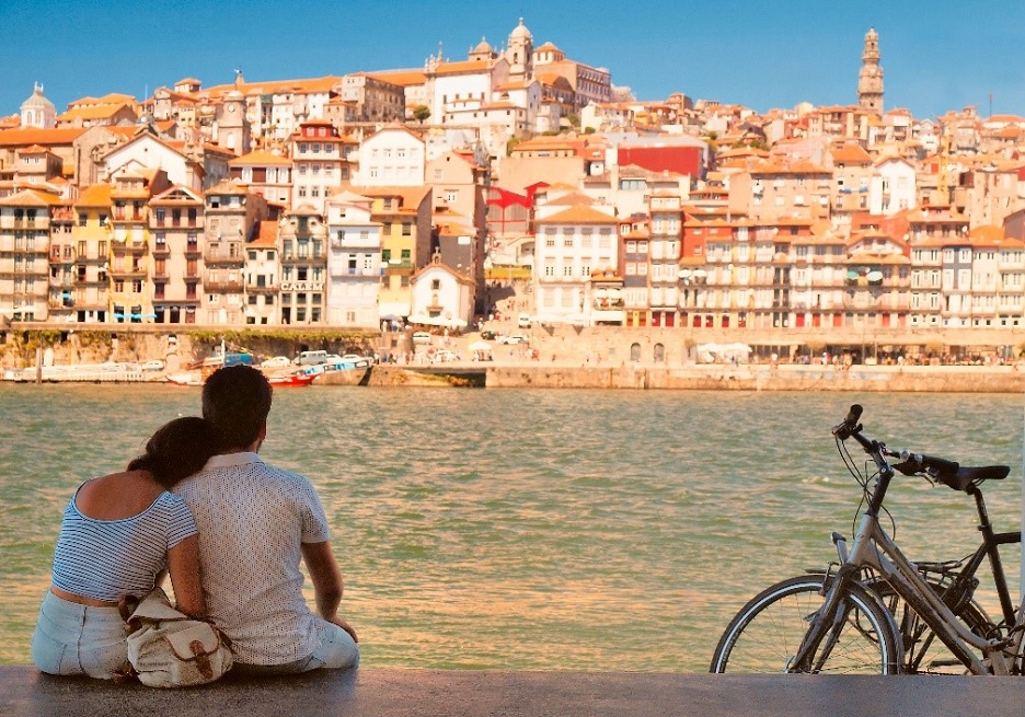 Pár sedieť na brehu rieky, hľadá naprieč v portugalskom meste na opačnej banky