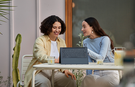 Two woman sitting on a table with a surface laptop