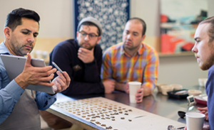 Four co-workers peer over a table at a tablet.