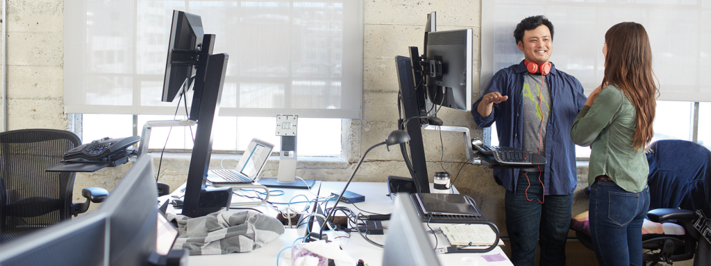 Image of two coworkers meeting next to a computer in their office.