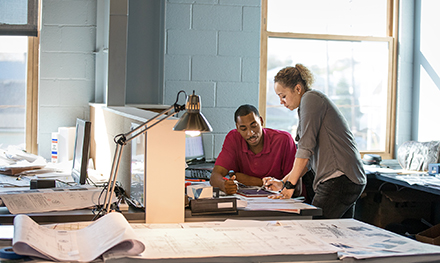 Two coworkers collaborate over a document on a desk.