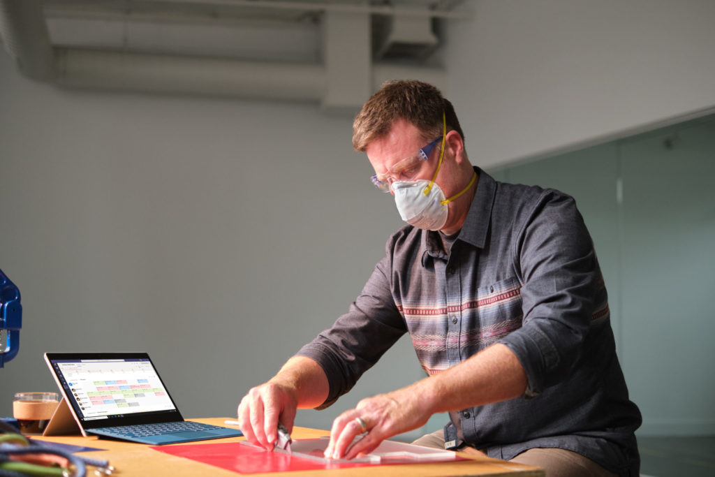 Manufacturing business owner wearing a mask and reviewing schedule in Shifts within Microsoft Teams.