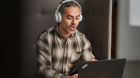 Un hombre sentado, usando auriculares mientras escribe en una computadora portátil.