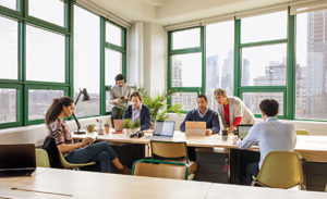 Image of a group of coworkers collaborating in a conference room, each on a variety of different devices.