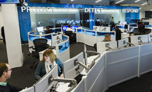 Image of a modern workplace. Above two workers speaking with one another are the words "Protect," "Detect," and "Respond."