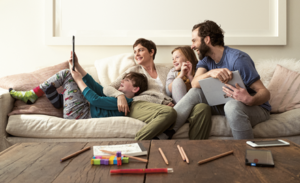 A family sits on a couch holding smart devices and laughing.