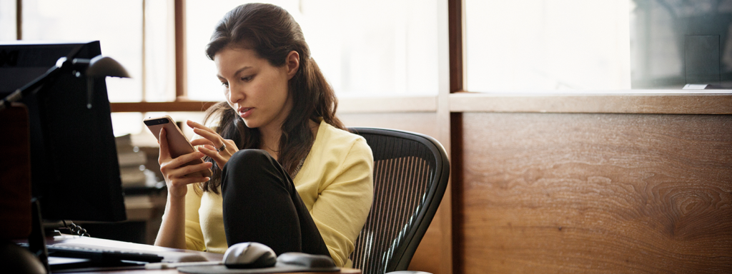 Image of a woman checking her phone while working at her desk.