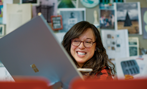 A firstline worker sits behind an open laptop, smiling during a meeting.