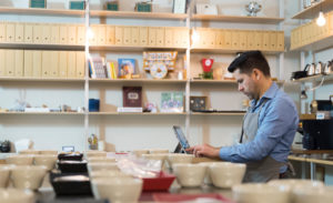 Image of a bakery owner and operator working on his laptop amid bowls and coffee cups.