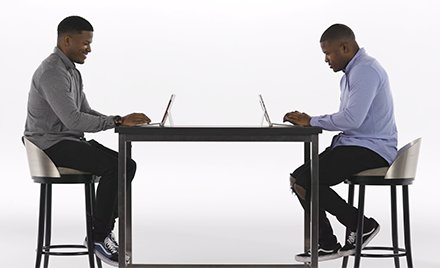 Image of twins sitting at a table, each with a laptop open.