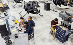 Image of workers assembling a helicopter. Several are gathered around a laptop.