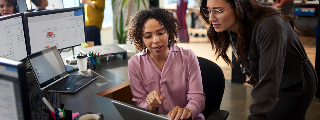 Image of two tech workers collaborating over a laptop.