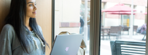 Image of a worker smiling out a window with her laptop open.