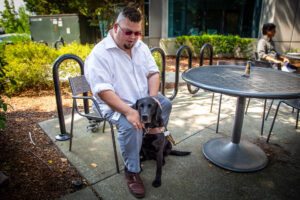 Cory Joseph sits at a table outside with his guide dog, Vine.