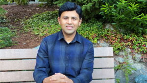 Guru Prasad sits at a bench, legs crossed, looking at the camera.