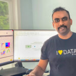 Kanamarlapudi sits next to a desktop and smiles with a shirt that reads “I love data.”