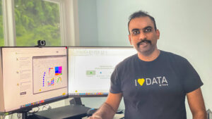 Kanamarlapudi sits next to a desktop and smiles with a shirt that reads “I love data.”