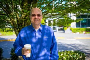 Apple holds a cup of tea as he smiles standing in front of a tree outside a Microsoft office.