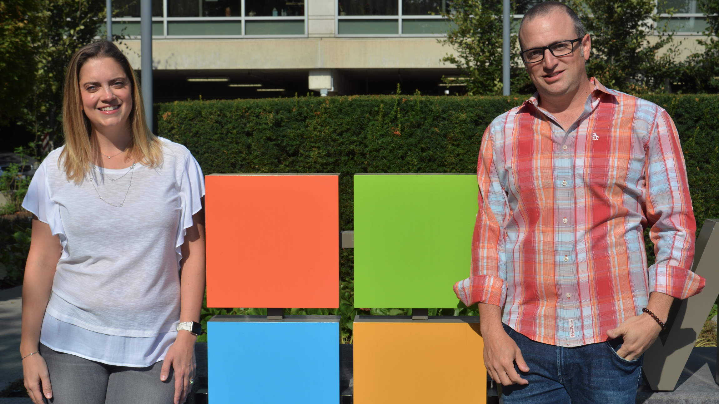 Yedinak and Laves stand and smile on either side of a Microsoft logo outside a Microsoft building.