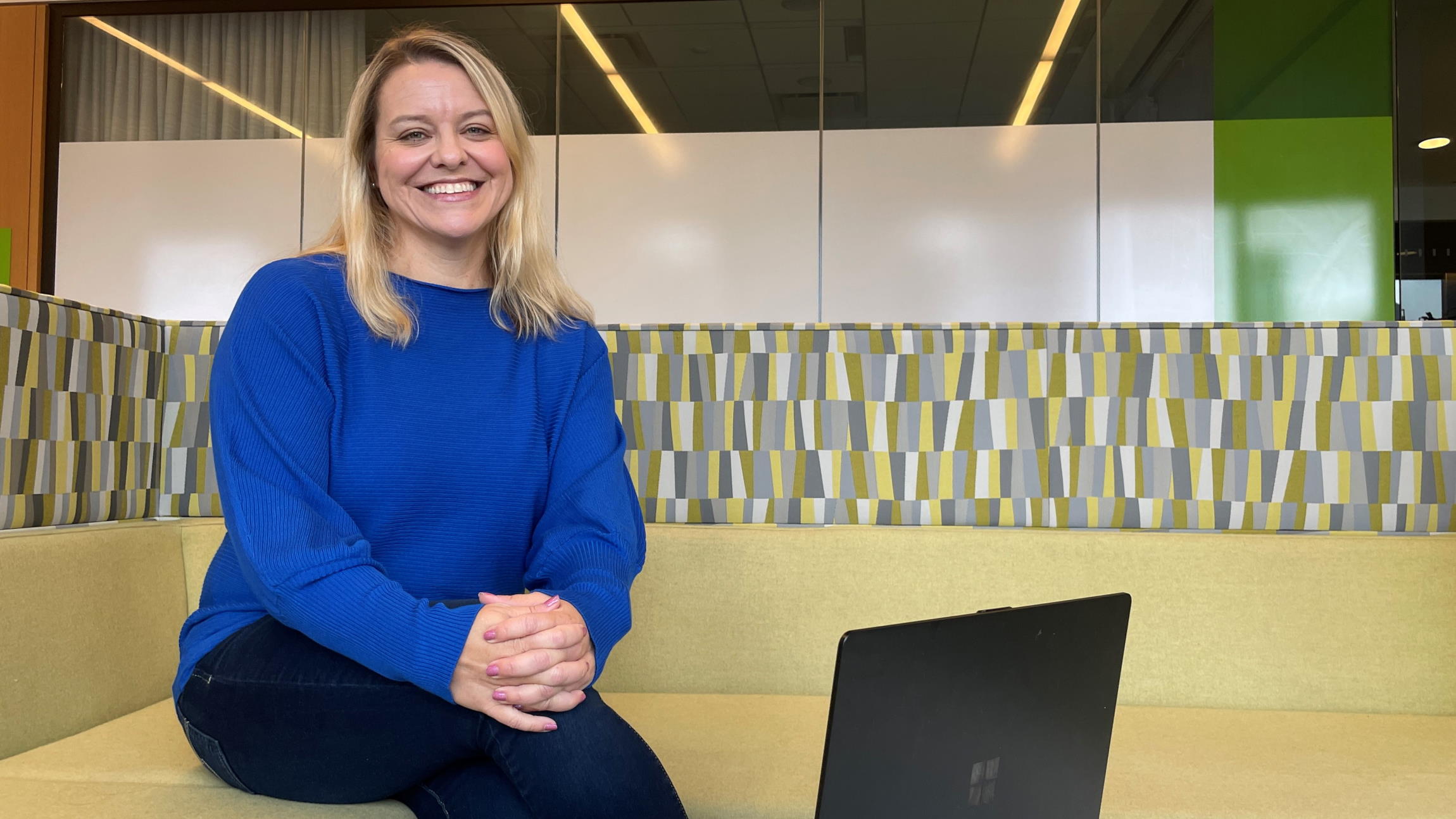 Kristin Burke sits smiling at the camera with her PC in front of her in a Microsoft office open space.