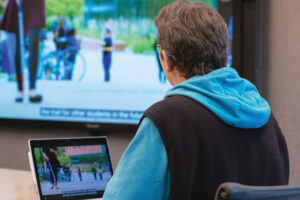 A woman who uses a hearing aid watches a video presentation with subtitles in a conference room.