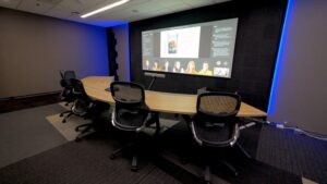 Meeting room with a table curving around and facing a wall display where virtual attendees and meeting content are shown together.