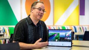 Crewdson sits in a Microsoft workspace showing off the capabilities of SharePoint on his laptop.