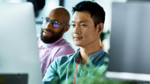 Two employees collaborate at a computer in a Microsoft office.