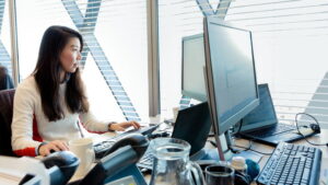 Female office worker looking at desktop monitor (screen not shown).