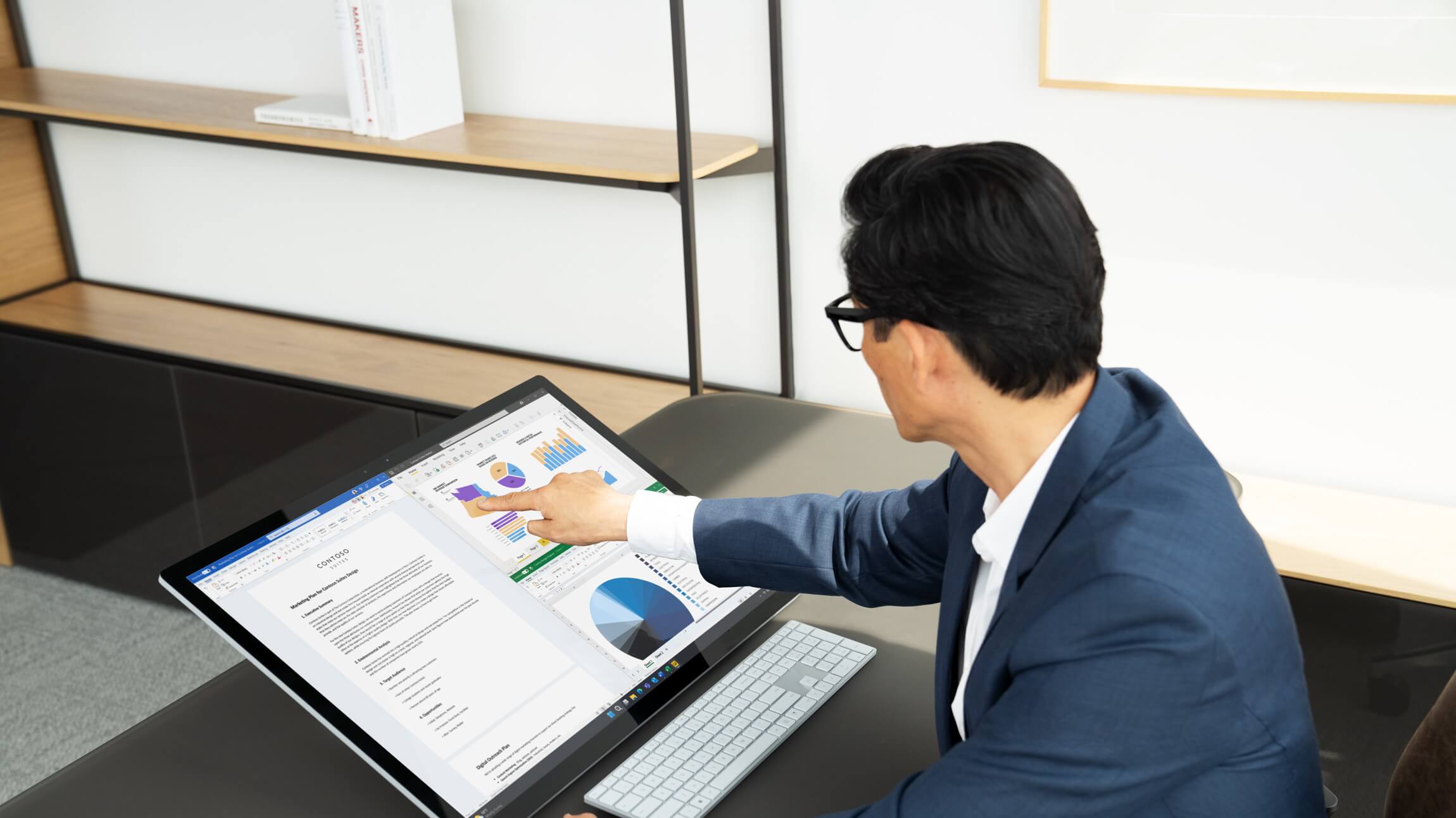 A professional in an office setting surveys an analytics dashboard on a Microsoft Surface Studio.