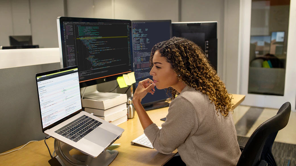 Black female developer working at enterprise office workspace. She has customized her workspace with a multi-monitor set up.