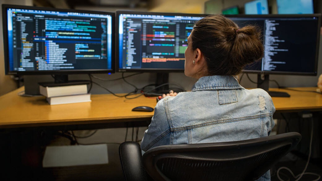 Female developer coding her workspace in an enterprise office, using a multi-monitor set up.