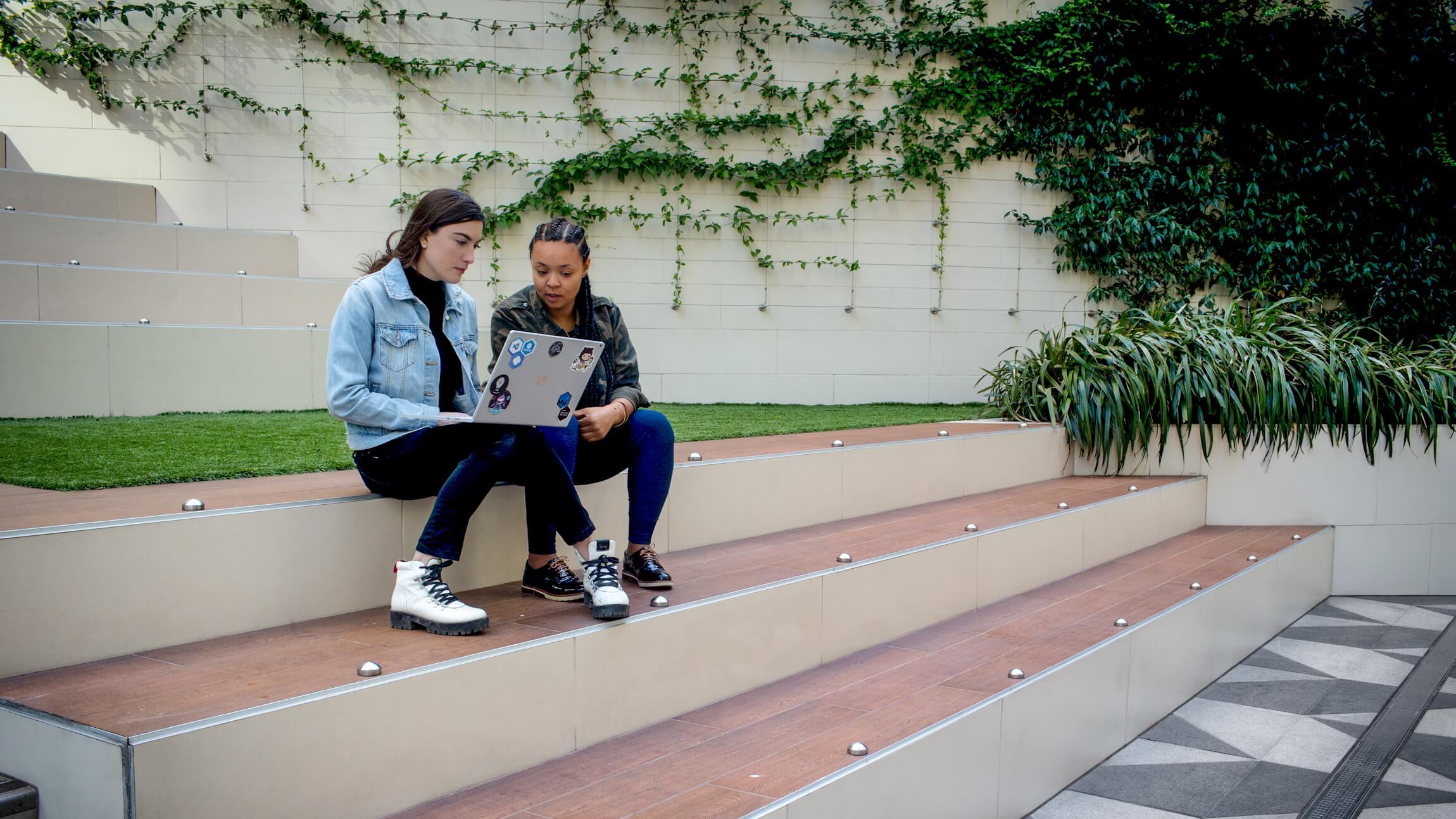 Close up of two female developers collaborating while working remotely. One developer has personalized her Surface laptop with stickers.