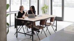 Two women talk in open office.