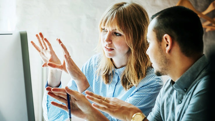 Two coworkers brainstorming in front of a computer screen.