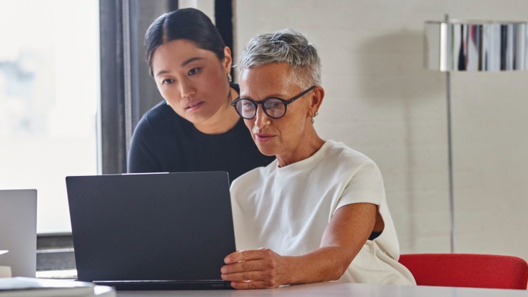 Two women at a desk with laptops open in conversation.