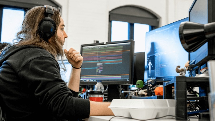 Programmer with headphones looks at several screens.