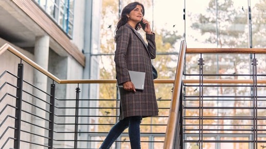 Woman on cell phone with laptop under her arm.
