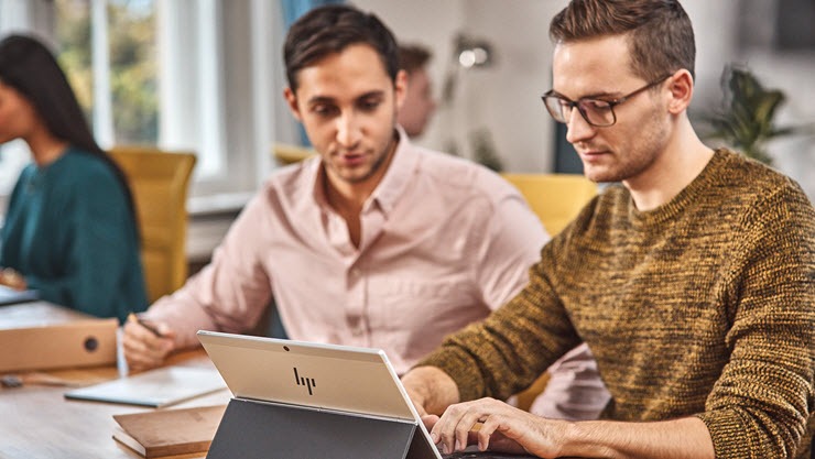 Two men in front of a laptop in an office setting.
