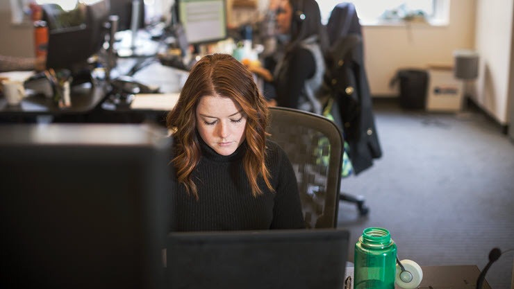 A woman, appearing deeply engrossed, is looking at her monitor.