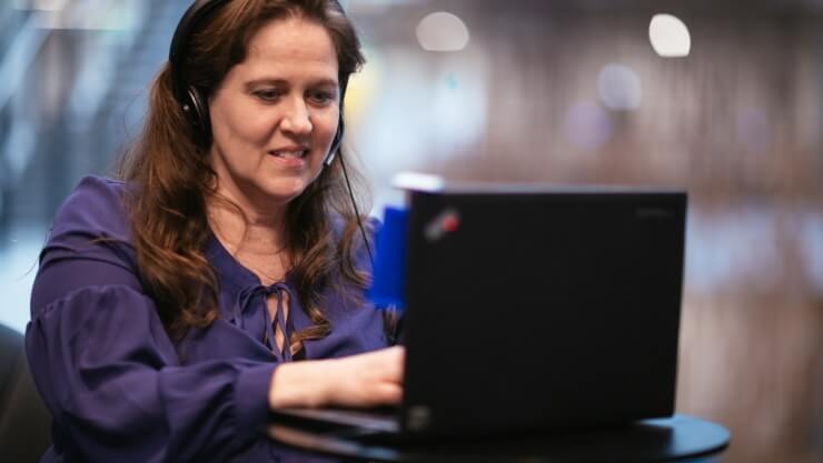 Debra Droz, a woman who is hard of hearing, wears headphones and types on a laptop.