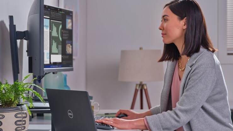 Business person uses a laptop connected to dual monitors at their home office.