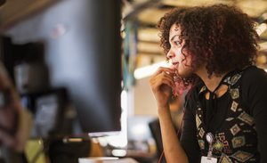 A woman with earbuds in looks at her computer screen.