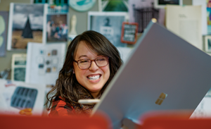 A firstline worker sits behind an open laptop, smiling during a meeting.