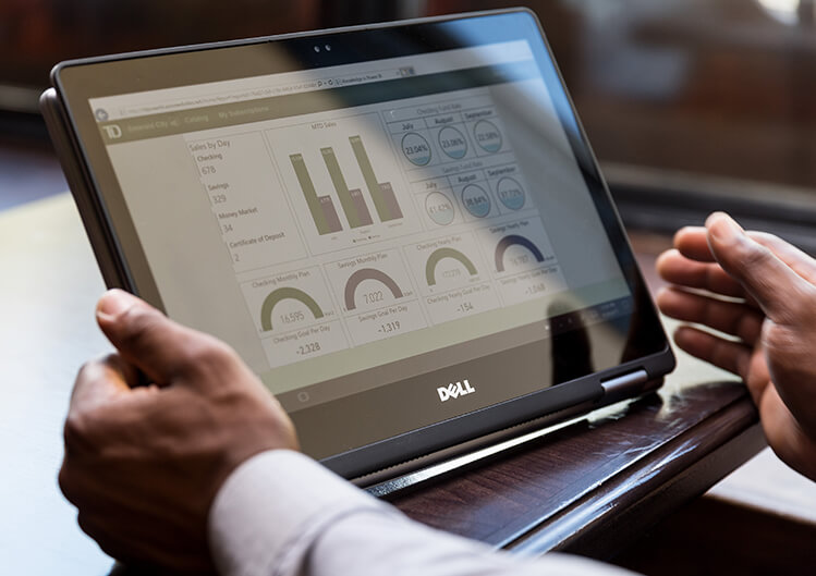 Close up shot of man‘s hands using Dell convertible laptop as tablet in café restaurant setting. Screen shows charts of TD Bank sales, savings, and checking accounts.