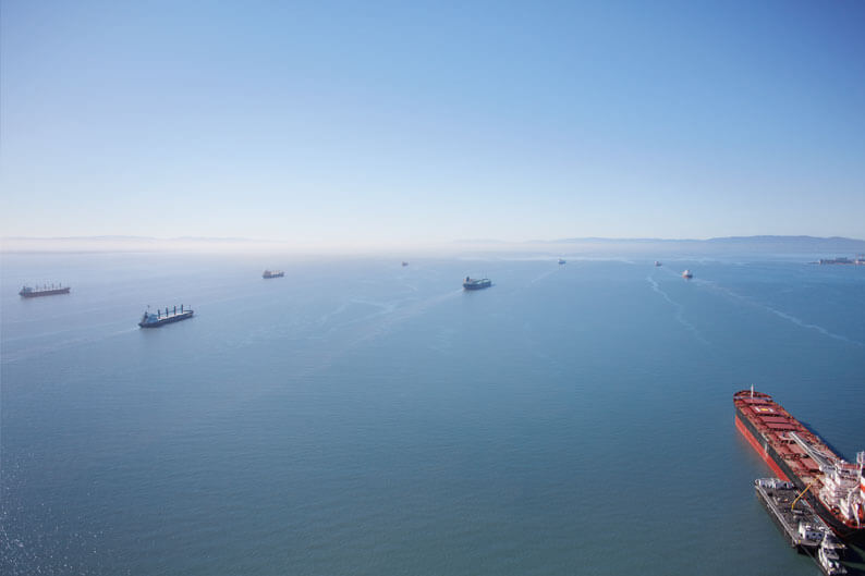 Aerial view of freighters in open sea with mountains in the background.