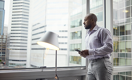 Image of a worker looking up from his phone to gaze out a window.