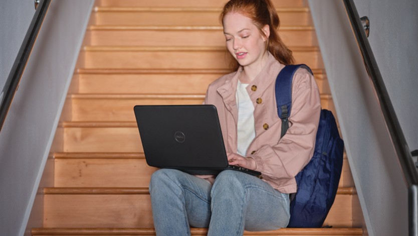 Uma garota com uma mochila sentada na escada com um notebook no colo